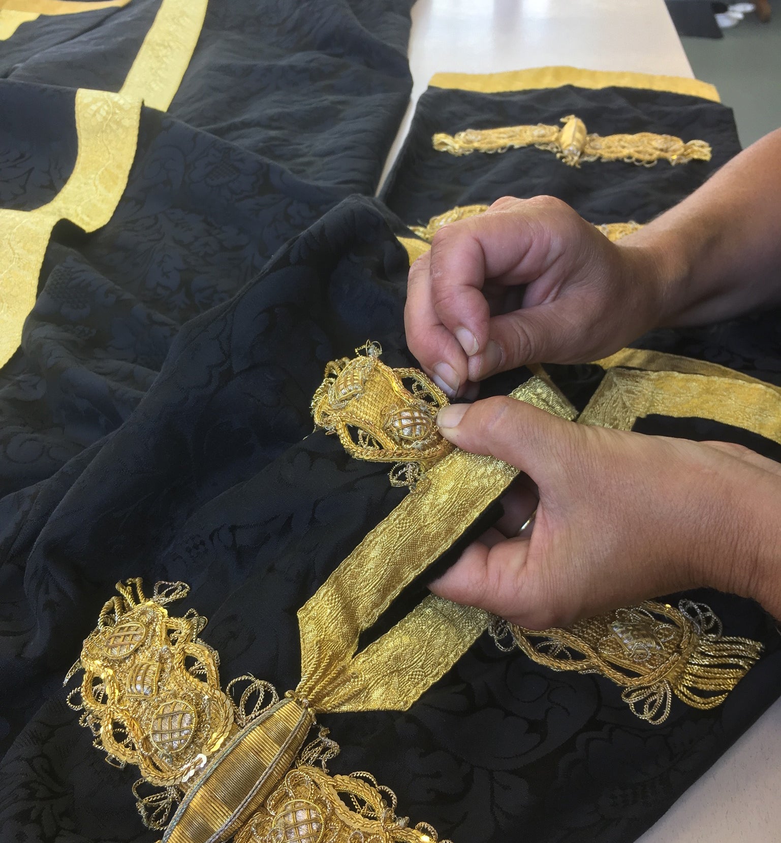 hand sewing gold frogging onto academic senior officers gown